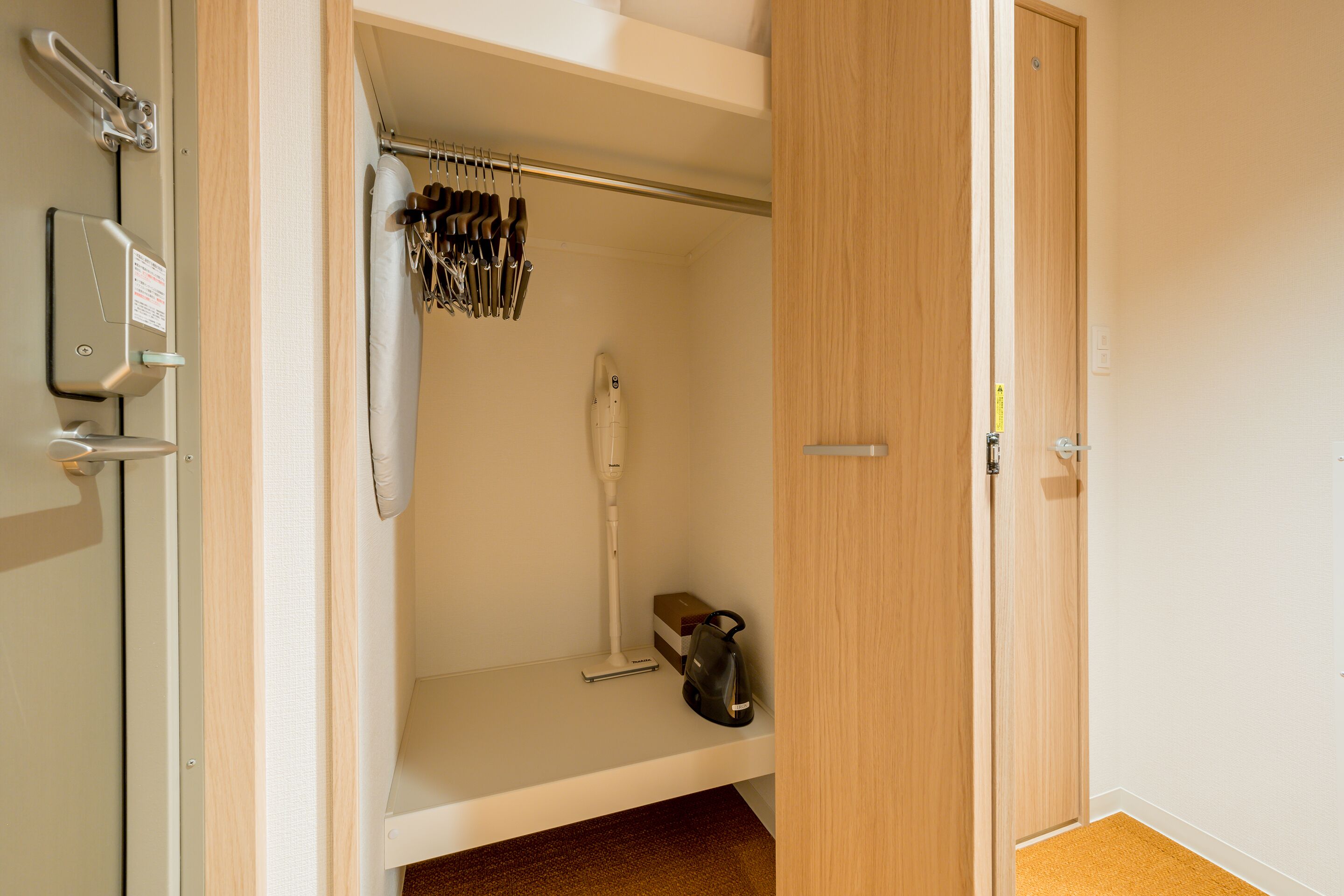 A room with a wooden door, a white towel hanging, and a shelf with various items including a vacuum cleaner.