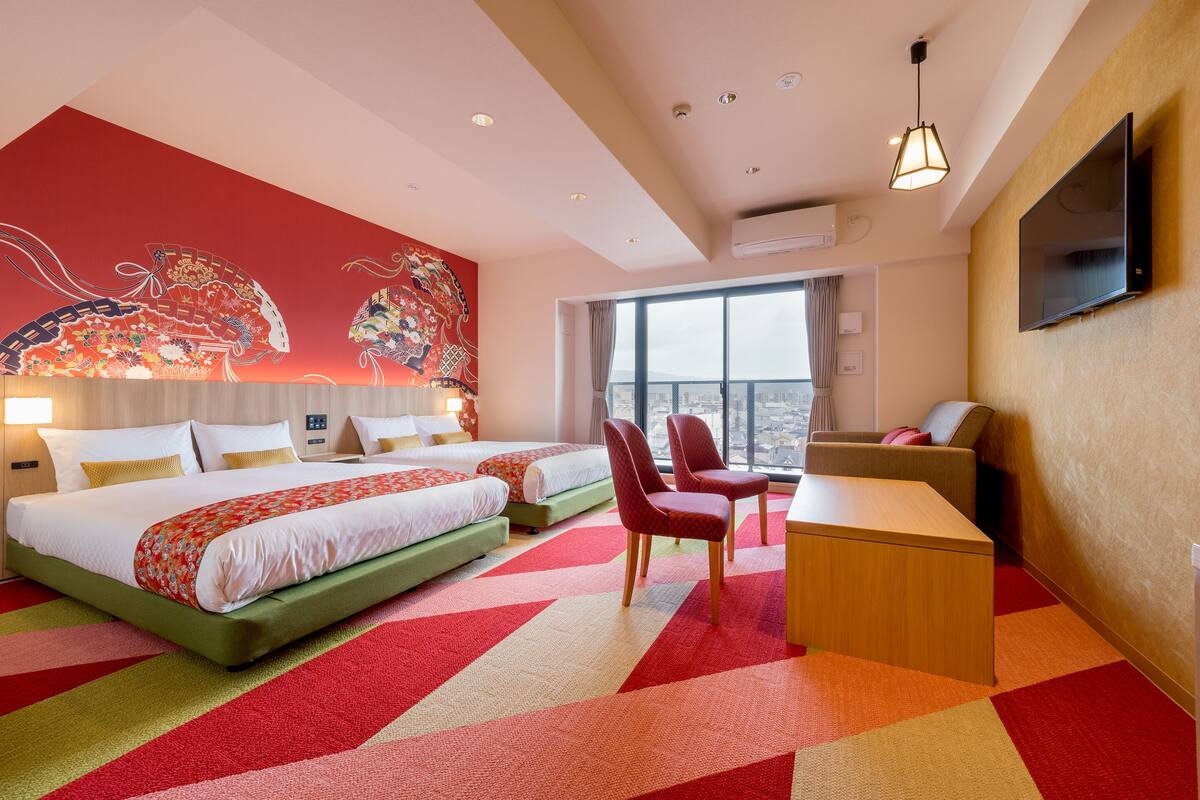 Ett hotellrum med två sängar, ett skrivbord, stolar, en TV och ett stort fönster.