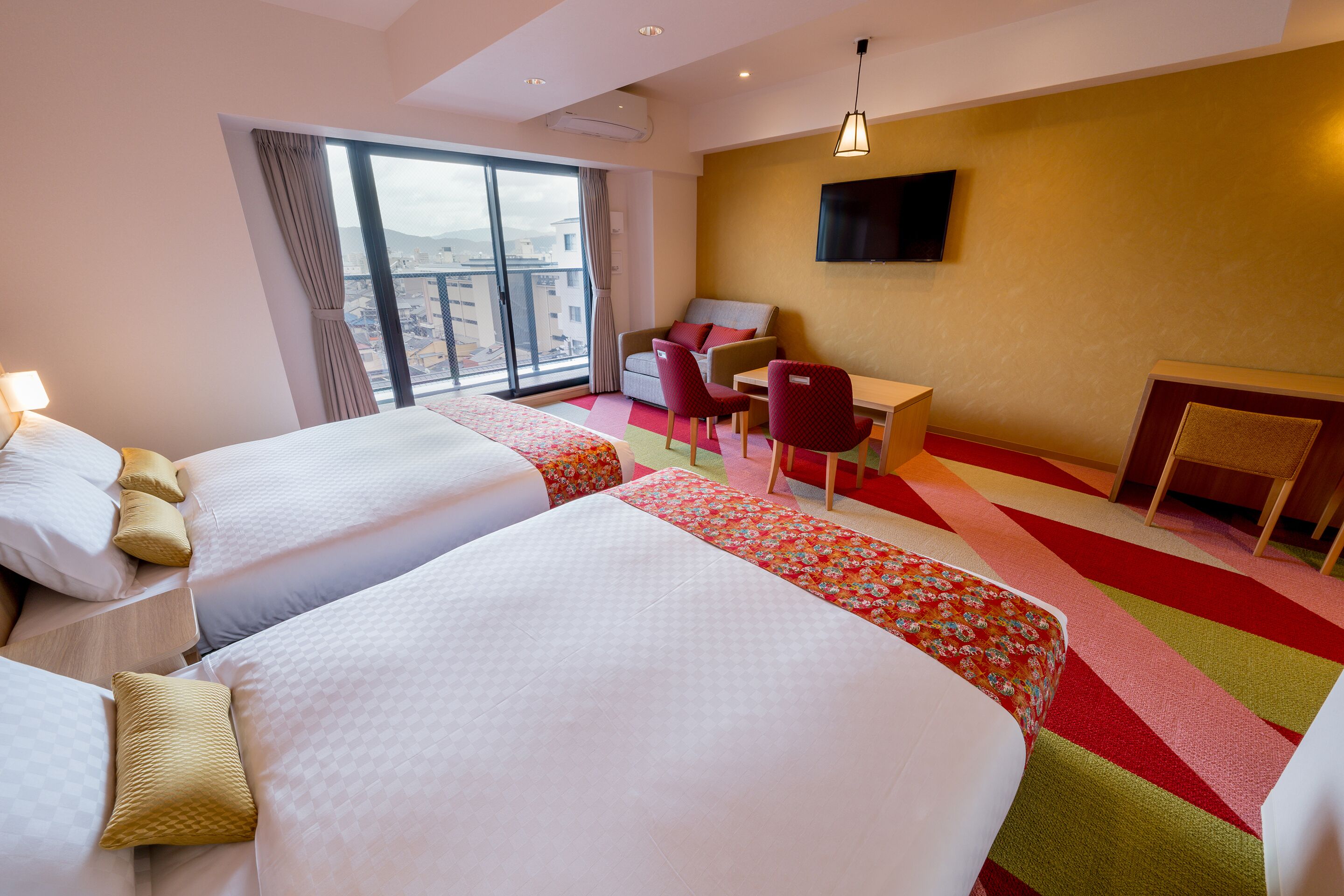 A hotel room with two beds, a desk, a chair, and a TV on the wall.