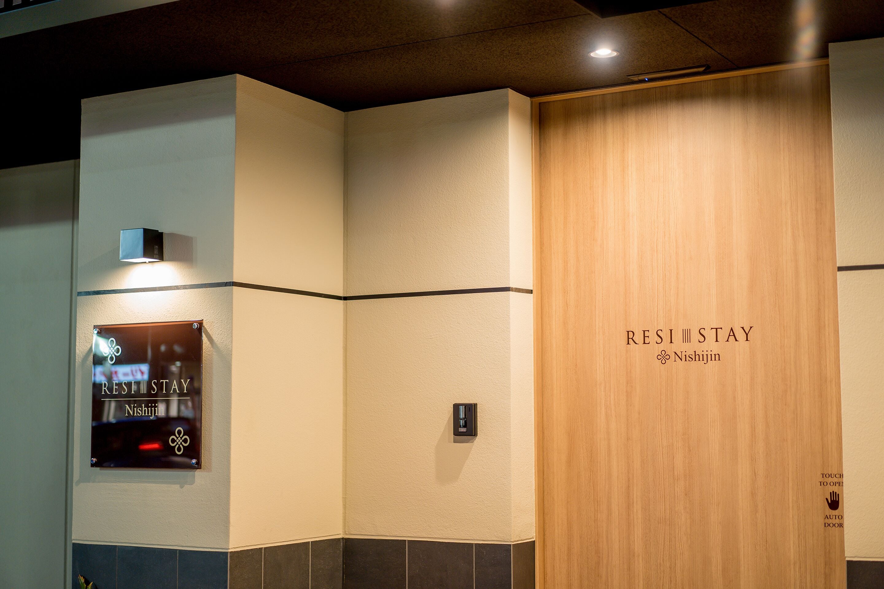Habitación de hotel con una puerta de madera que indica 'RESI STAY Nishijin'.