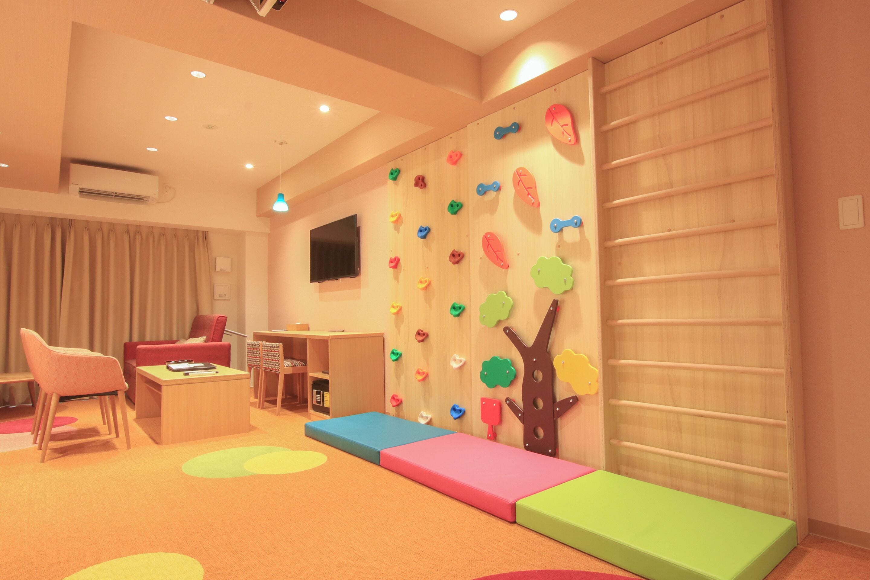 A room with a climbing wall, a desk, a chair, a bookshelf, and a window.