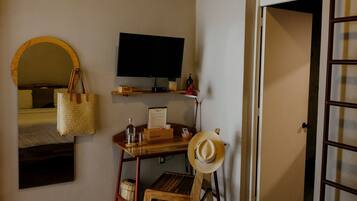 A bedroom with a bed, a desk with a chair, a television, an air conditioning unit, a wardrobe, and a door.