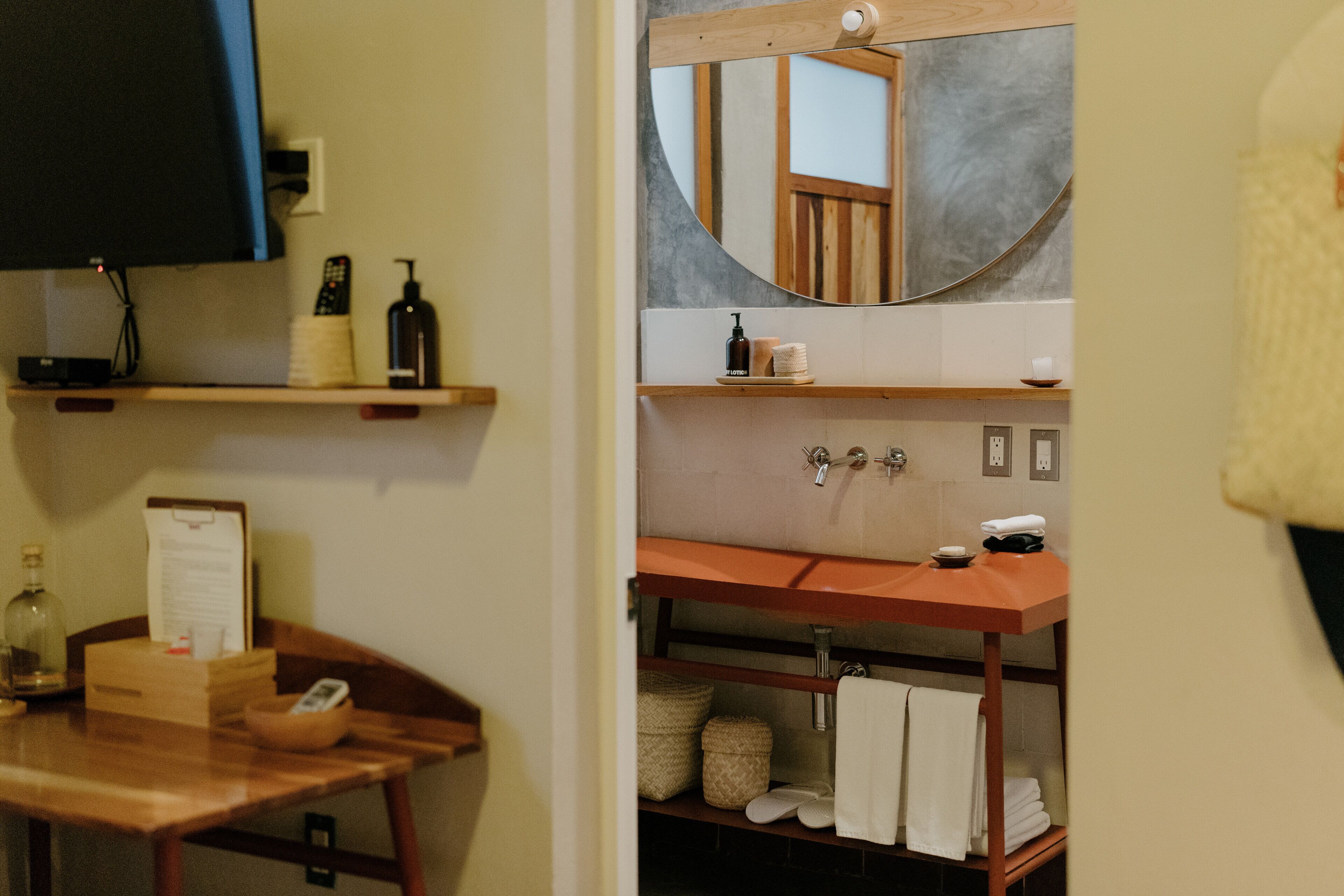 A bathroom with a wooden vanity, a large mirror, and a shelf with toiletries.