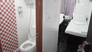 Un baño con pared de azulejos blancos y rojos a cuadros, un inodoro blanco, una zona de ducha y un lavamanos con espejo.