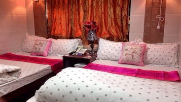 A hotel room with two beds, each with a pink bedspread, a nightstand with a telephone and a vase with flowers, and a curtain with a red and gold pattern.