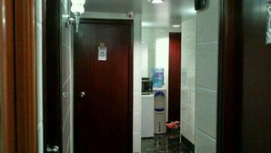 Un pasillo estrecho con una puerta de madera al final, un dispensador de agua y un refrigerador pequeño.