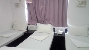 Una habitación de hotel con dos camas individuales, una mesita de noche con teléfono y una ventana con cortinas moradas.