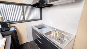 A compact kitchen with a built-in stove, a sink, and a window with blinds. - Kiyomizuya (Kyoto)