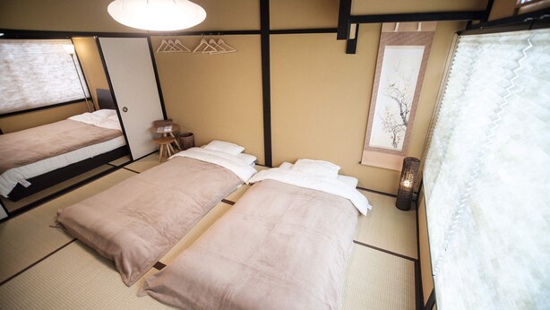 A traditional Japanese-style room with tatami flooring, two beds with pink bedding, a shoji screen, and a hanging light fixture. - Kiyomizuya (Kyoto)