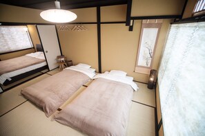 A traditional Japanese-style room with tatami flooring, two beds with pink bedding, a shoji screen, and a hanging light fixture.