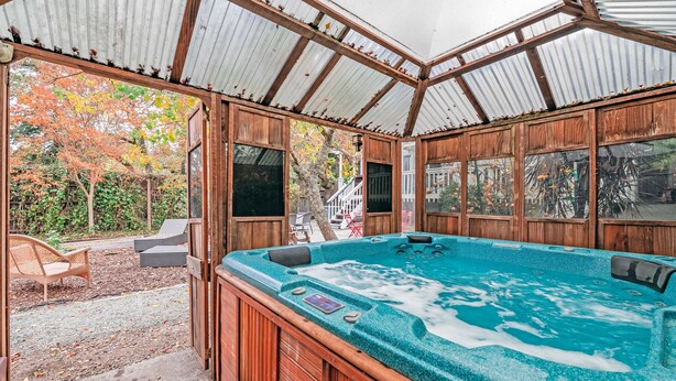 Een hottub in een houten blokhut met een overdekt terras en buitenmeubilair.