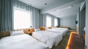 A hotel room with three beds, a wooden headboard, a bedside table, and a large window with curtains.