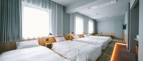 Una habitación de hotel con tres camas, cabecera de madera, una mesita de noche y un ventanal con cortinas.