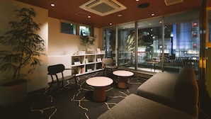 A modern lounge area with a sofa, two round tables, a bookshelf, and a large window offering a view of the city. - LANDABOUT TOKYO (Tokyo)
