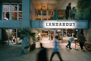 Un edificio moderno con un llamativo letrero 'LANDABOU'. Cuenta con un amplio espacio exterior con mesas y sillas, rodeado de plantas en macetas.