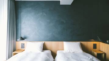 Une chambre d’hôtel moderne avec deux lits, une tête de lit en bois, un mur texturé de couleur sombre et une table de chevet avec une lampe.