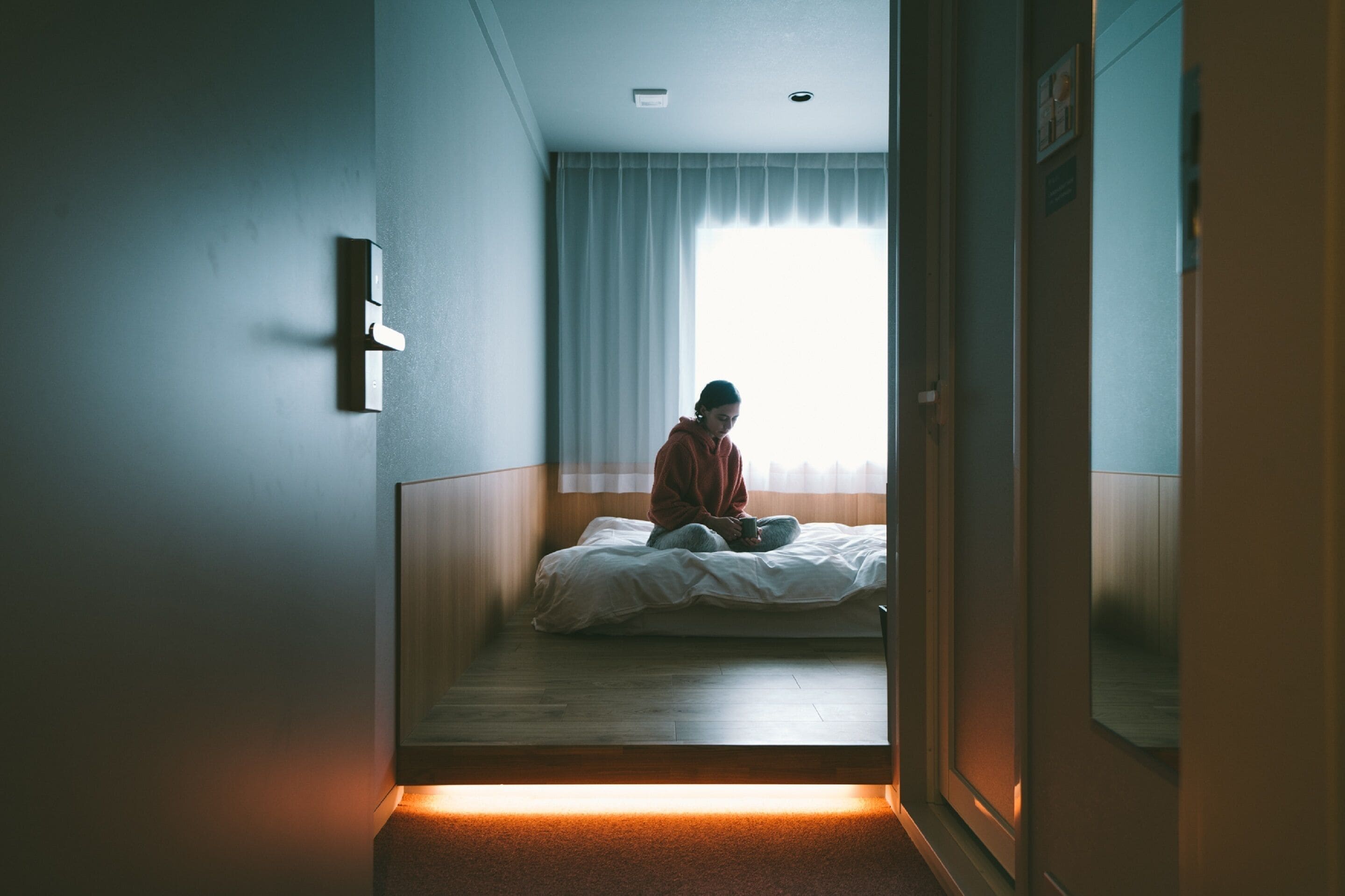 Un couloir étroit mène à une chambre à coucher qui contient un lit, une fenêtre avec des rideaux et une porte.