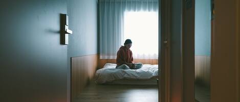 Un pasillo estrecho que conduce a un dormitorio con una cama, una ventana con cortinas y una puerta.