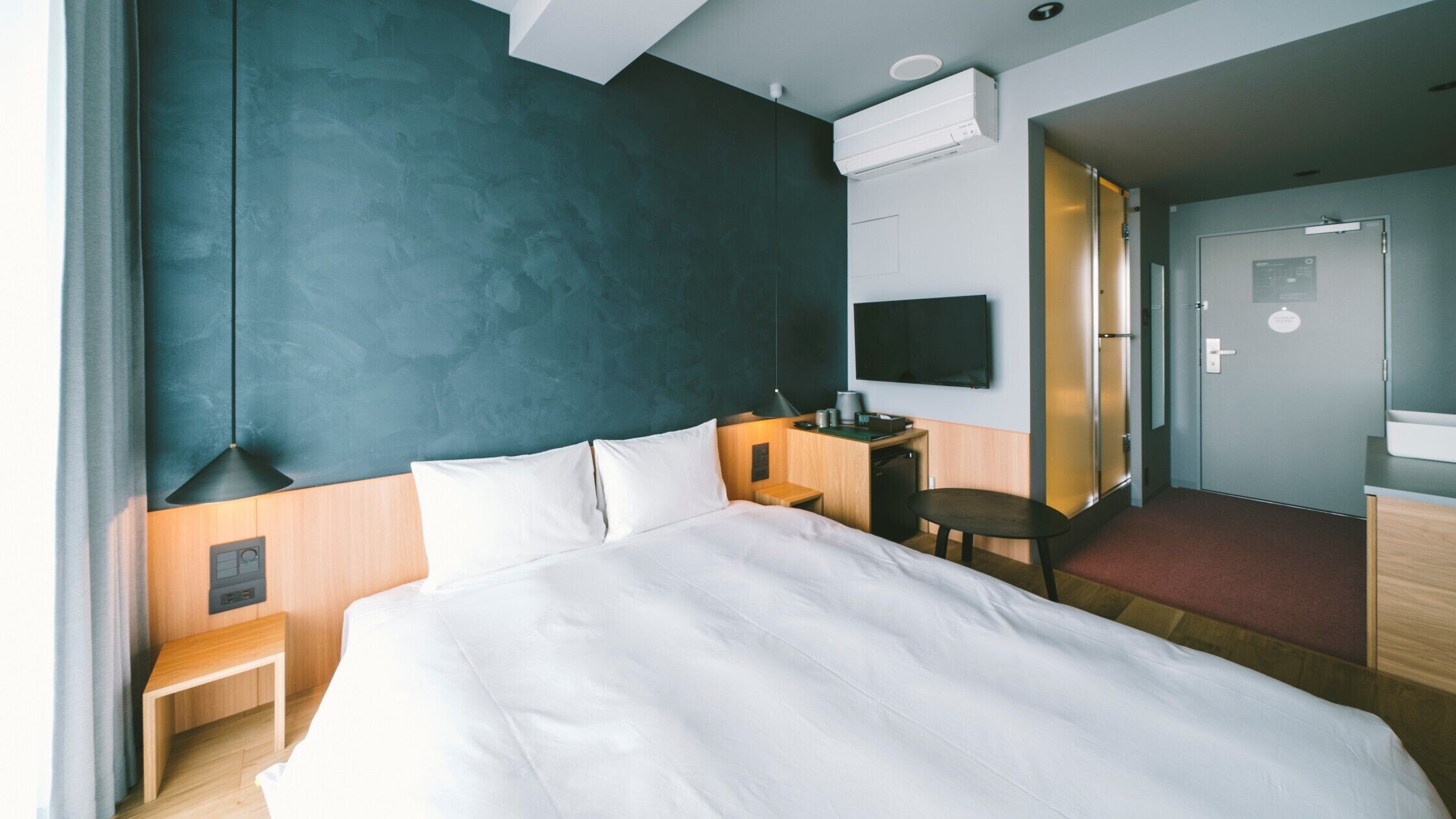 A hotel room with a large bed, a desk with a chair, a TV, and a door leading to another room.