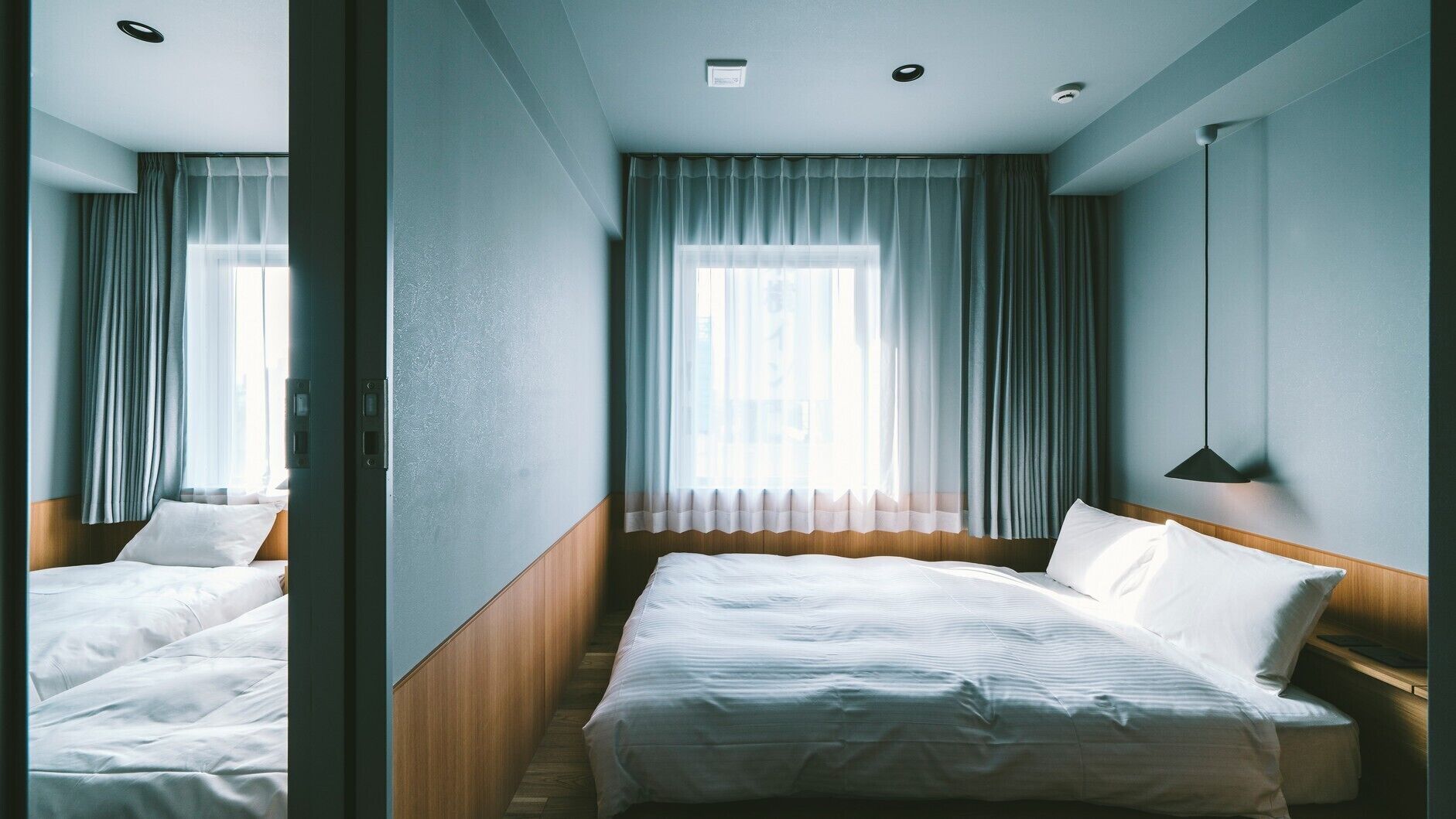 A hotel room with a bed, a bedside table, a lamp, and a window with curtains.