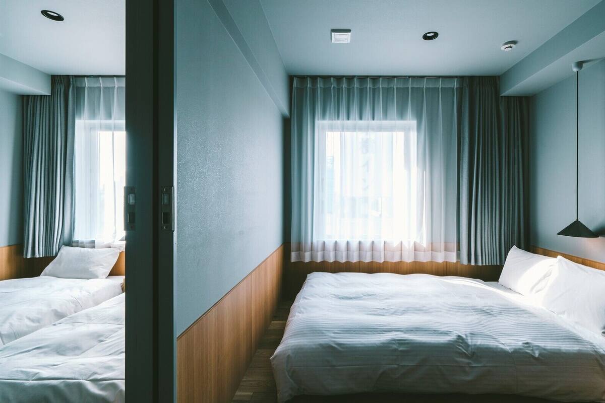 A hotel room with a bed, a bedside table, a lamp, and a window with curtains.