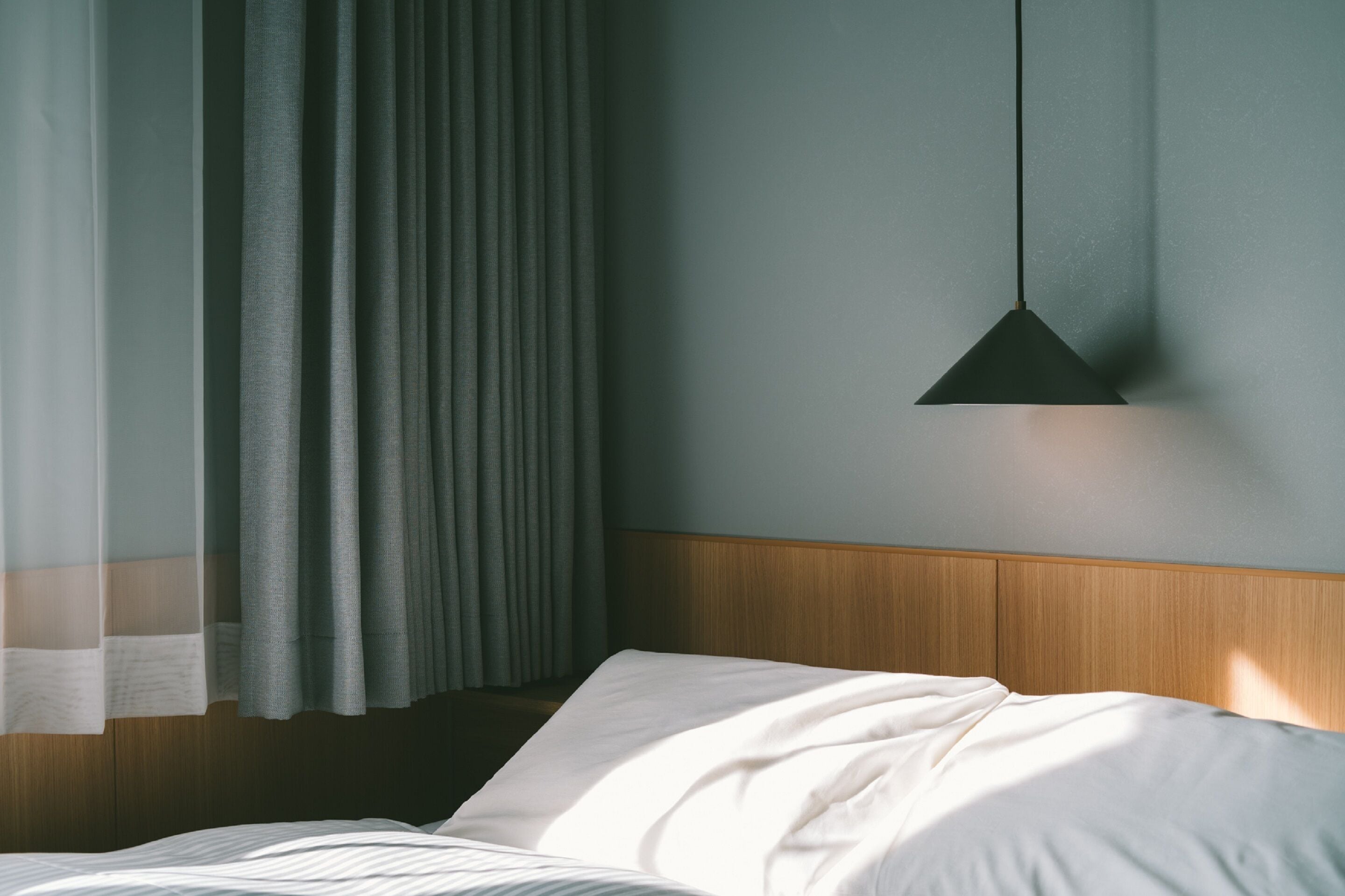 A hotel room with a bed, a wooden headboard, and a hanging pendant light.