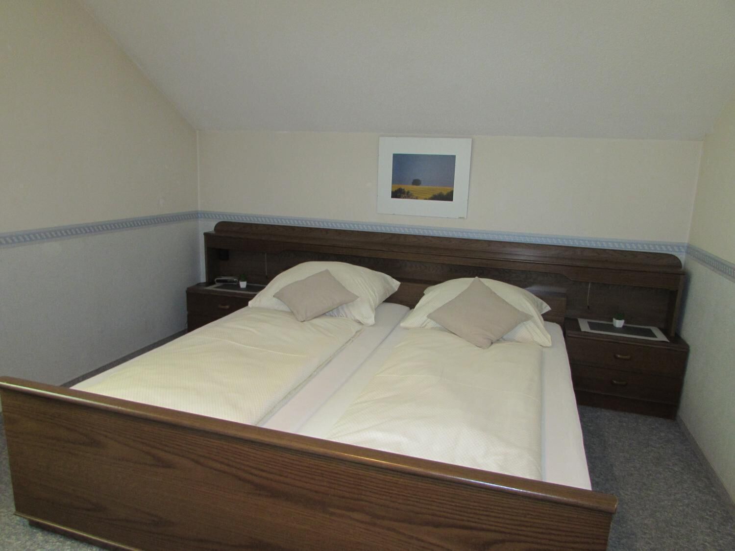 Una cama doble con cabecera de madera, dos mesitas de noche y un pequeño marco de fotos en la pared.