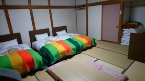 A traditional Japanese-style room with tatami flooring, two beds with colorful bedding, and a wooden wardrobe. - Apple Inn Takasaka (Nozawaonsen)