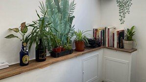 A corner room with a wooden shelf holding potted plants, a radiator, and a window with curtains. - Hop Inn - Hostel (Kowloon)
