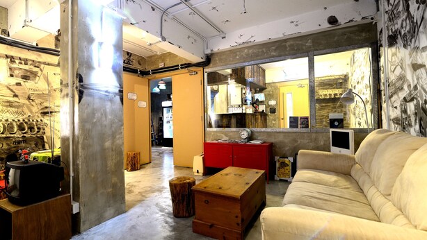 A room with a wooden chest, a red cabinet, a beige sofa, and a large mirror reflecting a yellow door and a clock. - Hop Inn - Hostel (Kowloon)