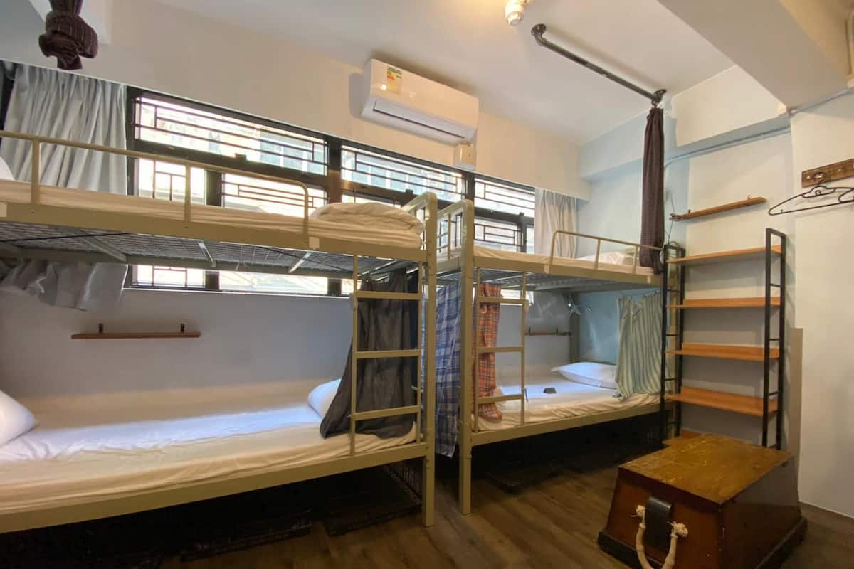 A dormitory room with bunk beds, a wooden chest, and a ladder.
