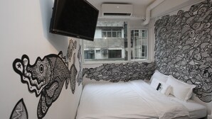 A bedroom with a bed, a TV mounted on the wall, and a window with a view of buildings. - Hop Inn - Hostel (Kowloon)