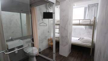 A compact hotel room with a shower, toilet, and a bunk bed.