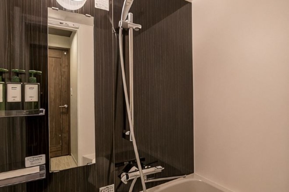 A bathroom with a shower, a mirror, and toiletries on a shelf.