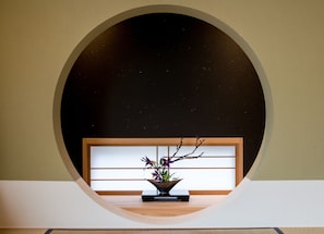 A minimalist room with a circular window, a wooden bench, and a potted plant with purple flowers.