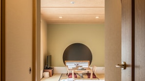 Ein traditionell eingerichteter japanischer Raum mit Tatami-Boden, einem Bett mit niedrigem Kopfteil, einem Fernseher und einem kleinen Tisch mit Stuhl.