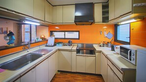 A compact kitchen with a sink, stove, microwave, and orange-tiled backsplash. - Yoshimura House Hotel 5 (Fujikawaguchiko)
