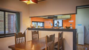 A dining area with a wooden table and chairs, a kitchen with orange tiles, and a refrigerator. - Yoshimura House Hotel 5 (Fujikawaguchiko)