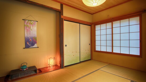 A traditional Japanese room with tatami flooring, sliding shoji doors, a hanging shoji screen, and a small table with a teapot. - Yoshimura House Hotel 5 (Fujikawaguchiko)