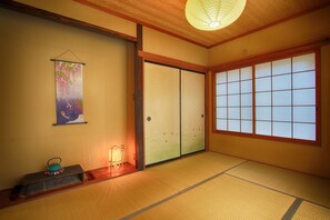 Ein traditioneller japanischer Raum mit Tatami-Böden, gleitenden Shoji-Türen, einer hängenden Shoji-Trennwand und einem kleinen Tisch mit Teekanne.