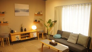 A living room with a sofa, a coffee table, a lamp, a plant, and a painting on the wall. - Yoshimura House Hotel 5 (Fujikawaguchiko)