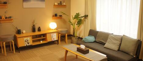 Una sala de estar con sofá, mesa de centro, lámpara, planta y un cuadro en la pared.