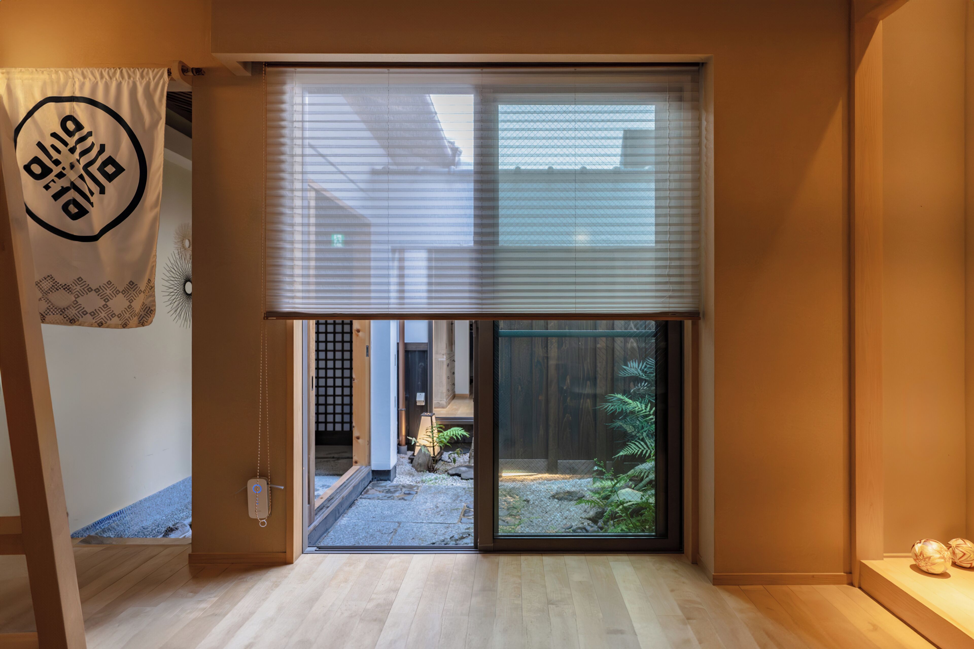 A room with a sliding door leading to a garden, a wooden floor, and a wall-mounted sign.