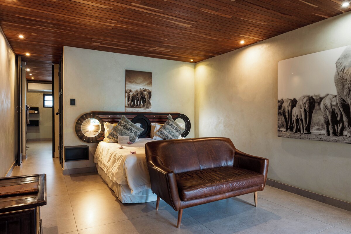 A bedroom with a bed, a brown leather chair, and two wall-mounted artworks.