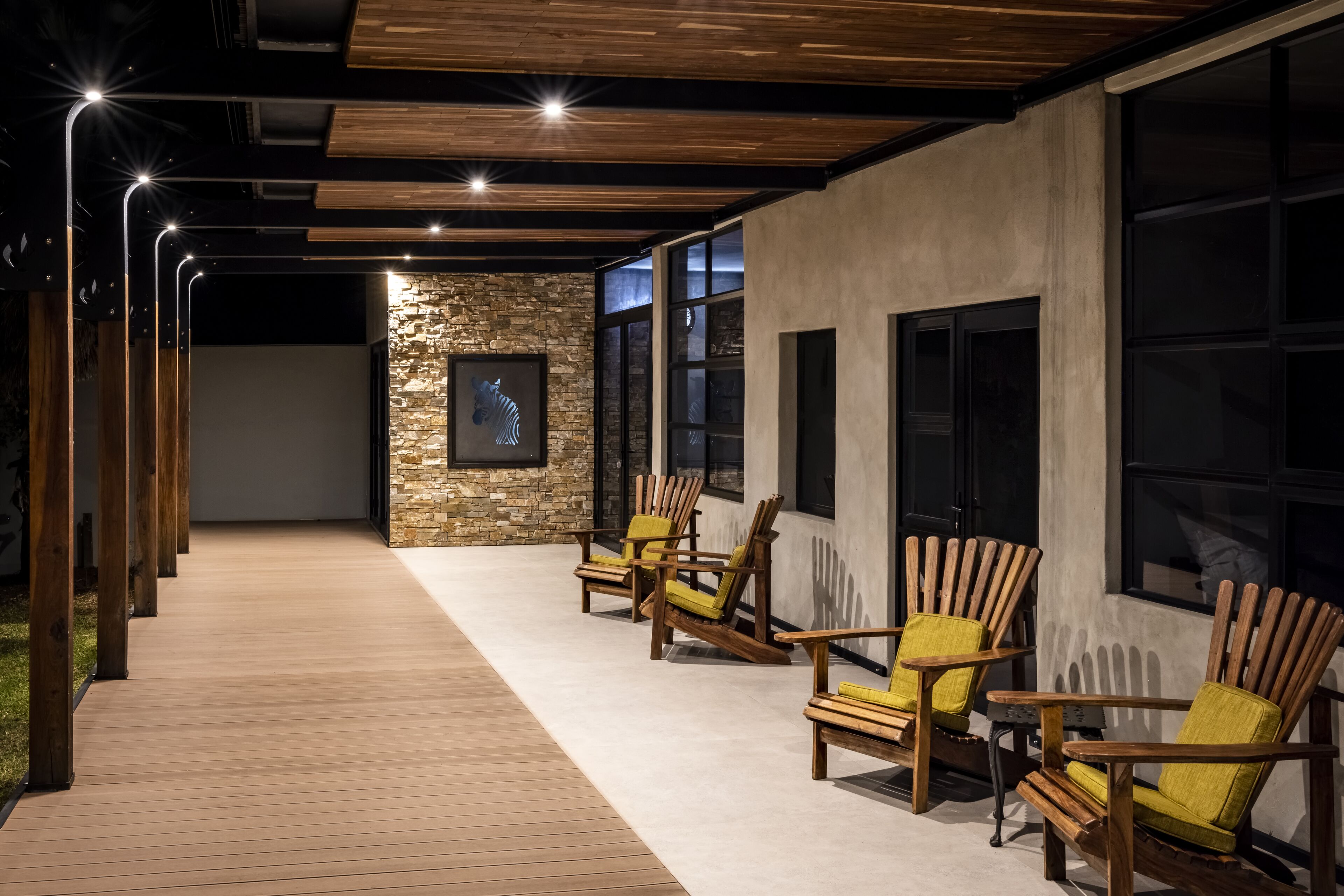 Un área de estar al aire libre con techo, sillas de madera y una pared de piedra.