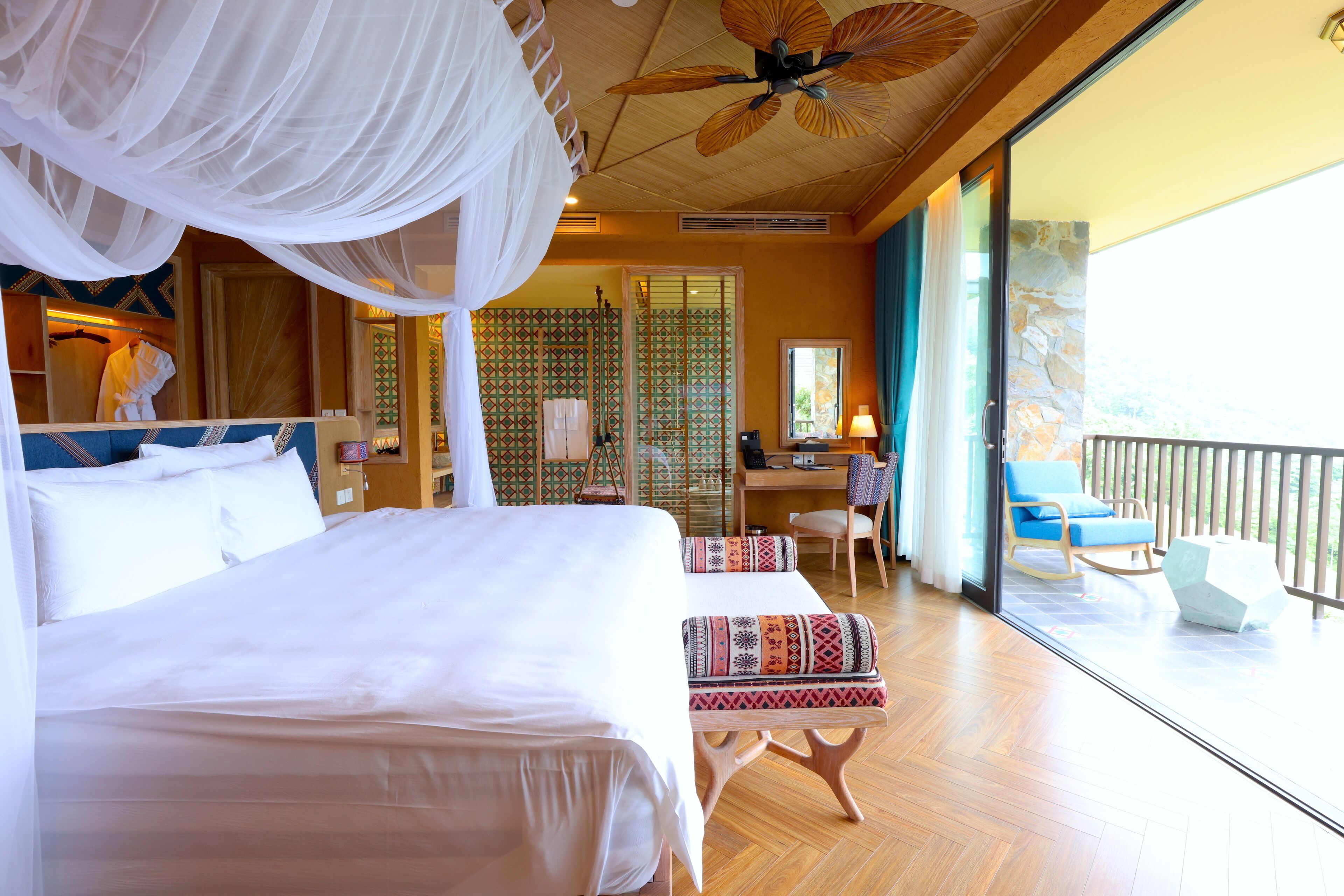 A bedroom with a large bed, a desk, and a balcony with a chair.