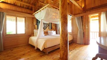 A wooden cabin bedroom with a four-poster bed, a wooden floor, and a large window.