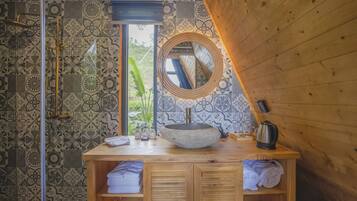 Un baño con tocador de madera, espejo redondo, lavabo de piedra y zona de ducha con azulejos estampados.