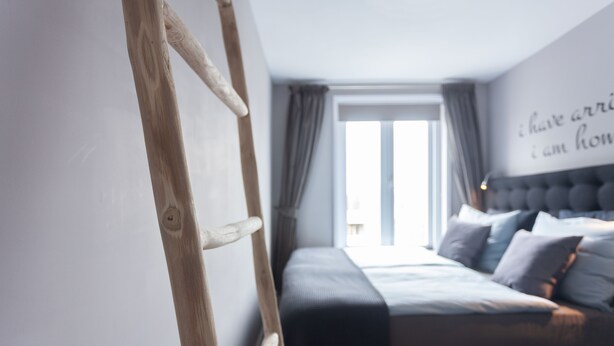 A bedroom with a bed, a wooden ladder, a window with curtains, and a wall with a partial text. - Bed and Breakfast The Rose (Haarlem)