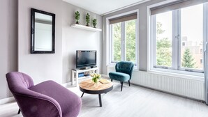 A modern living room with a large window, a flat-screen TV, a round coffee table with a vase, and two chairs. - Bed and Breakfast The Rose (Haarlem)